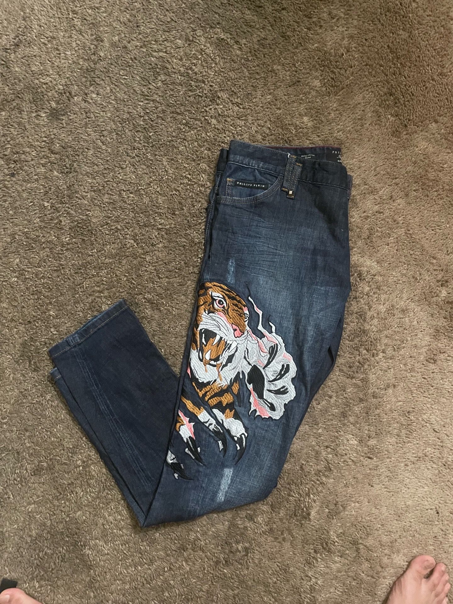 Philipp Plein jeans feature a prominent, colorful embroidered tiger design on the right leg.
