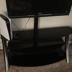 Three-tier TV stand made of black glass and silver sides holds the TV