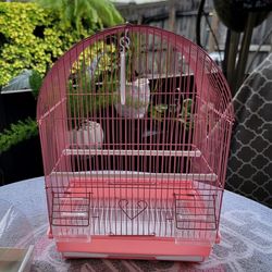 Pink bird cage with a white base. Includes a water dispenser, a food dispenser, and three climbing accessories.