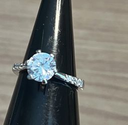 Elegant silver ring featuring a brilliant white round center stone. Classic solitaire style with sparkling white accent stones on the band. Timeless
