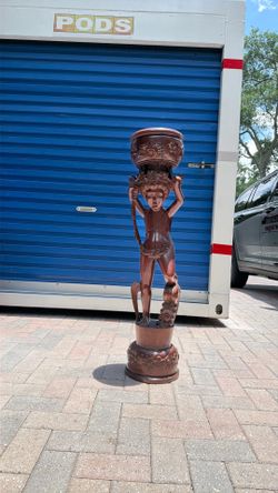 Hand carved wooden pedestal, stand featuring cherub holding a bowl on his head. Vintage. Most likely made of mahogany Cherrywood and stained with oxbl