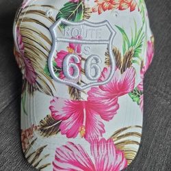 Tropical hibiscus print baseball cap is made of 100% acrylic material. Hat has white background with pink and orange floral pattern and green leaves. 