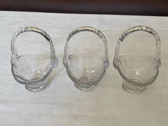A set of three clear, pressed glass miniature baskets with handles.