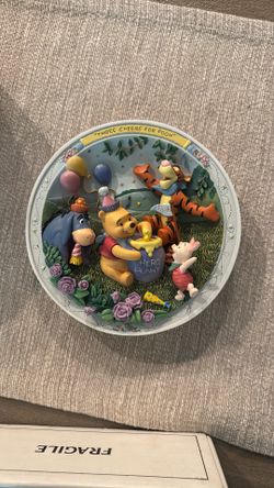 A collectible 3D plate featuring Winnie the Pooh characters, titled 'Three Cheers for Pooh'.