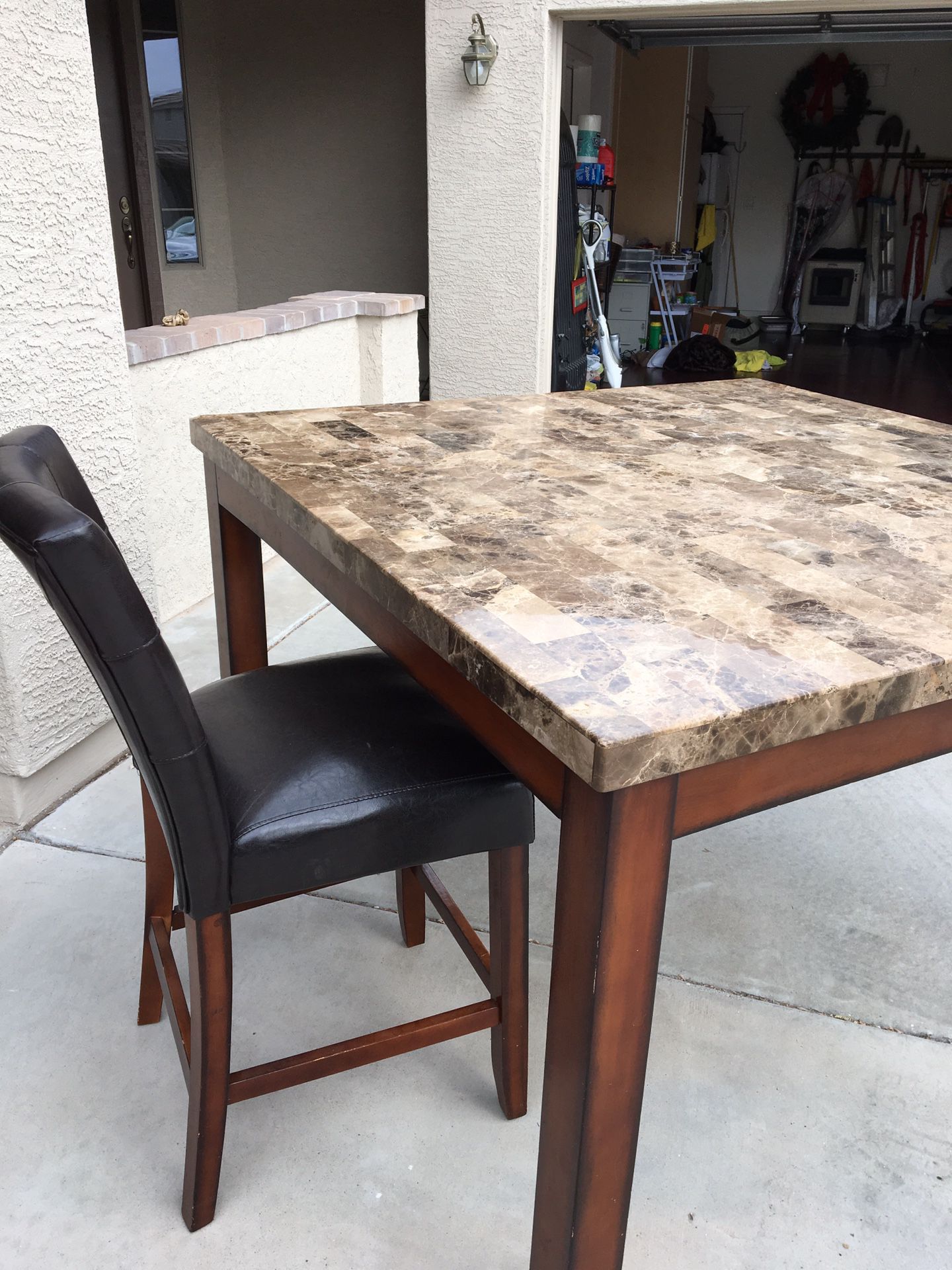 Kitchen/dining table. Solid granite top with small chip on top corner. 4 dark brown leather like chairs. Table measures 54” square.