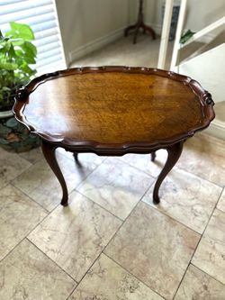 vintage French Country-style oval occasional tea table features a scalloped gallery edge and graceful cabriole legs.