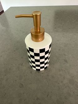 This soap dispenser has a classic checkerboard pattern. It features a gold pump and a white and black body. It's great for kitchens or bathrooms!