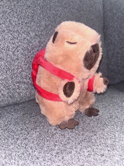 sleeping capybara plush toy with a red backpack