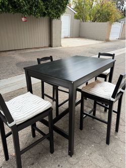 A black dining table with four bar height, chairs in good condition