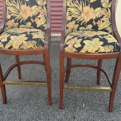 pair of wooden bar stools with upholstered seats and backs featuring a black background with a tropical leaf and floral pattern  22” wide    19 1/4” d