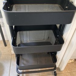 Three-tier black metal rolling cart with mesh trays.