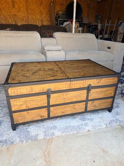 This is a rustic wooden storage trunk coffee table featuring dark metal trim and casters.
