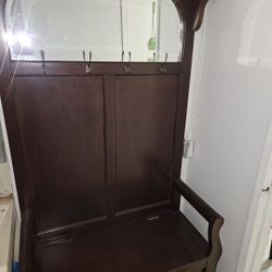 A wooden entryway coat storage bench with mirror