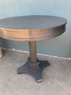 A modern round pedestal dining table with  a dark silver finish.