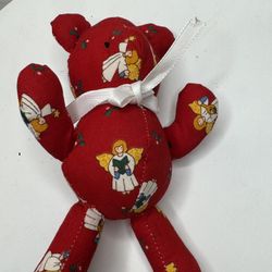 A small plush teddy bear made of red fabric with an angel pattern