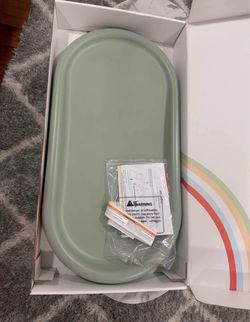 Pristine sage green changing pad is made of a smooth, wipeable material. This Milou Stay Clean model includes the original packaging, safety strap, an