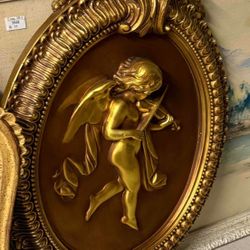Gilded relief cherub playing violin wall plaque in ornate frame.