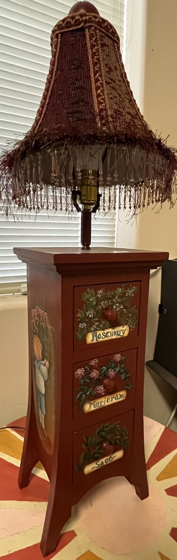 Decorative lamp with a fringed- jeweled shade featuring small pull drawers w hand painted lettering/herb shrubbery and girl & boy on side of