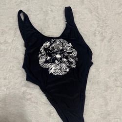 Black one-piece swimsuit with a bold silver metallic dragon print. Sleek scoop neckline and supportive straps for a secure fit. Smooth, stretch fabric