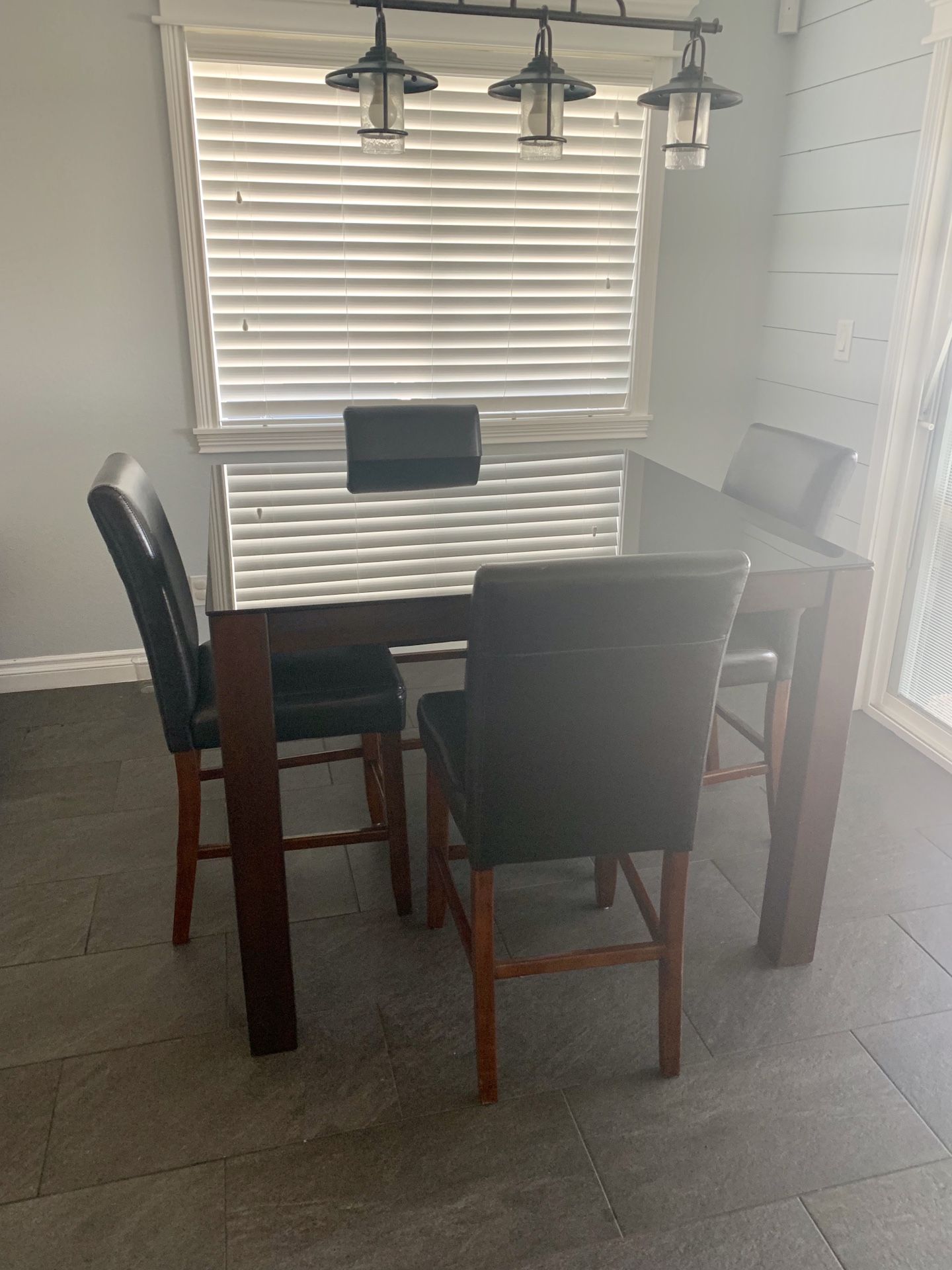 Tall glass top kitchen table with dark wood legs and 4 faux vinyl cushion chairs