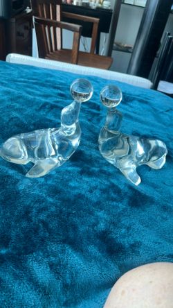 A pair of clear art glass seals, each balancing a ball on its nose.