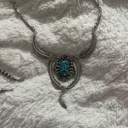 This necklace is a Southwestern or Native American-style silver and turquoise necklace featuring prominent feather and scroll motifs. It combines elem