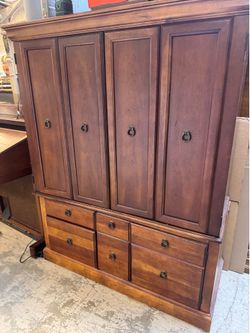 armoire features dark cherry wood construction with classic raised paneled doors and distinctive antique-style ring pulls