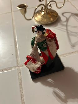 vintage Japanese geisha or kimono doll figurine mounted on a black wooden base. • Subject: Handcrafted Japanese female figure wearing a patterned kimo