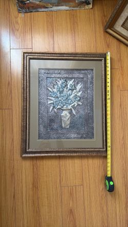 Decorative embossed metal wall art piece (often aluminum, pewter-toned metal, or mixed-media relief art) featuring a floral arrangement in a vase.