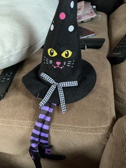 black cat witch hat decoration featuring purple and black striped dangling legs and witch shoes.