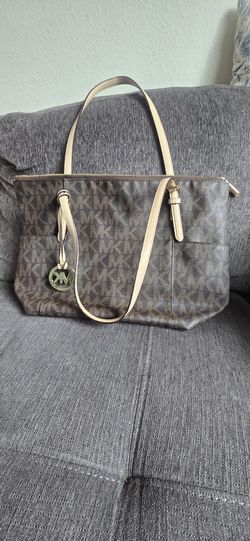 Classic Michael Kors tote bag has brown monogram coated canvas with tan leather straps. Interior is lined with signature fabric and includes multiple 