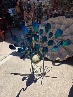 Decorative metal peacock garden sculpture with green and blue feathers.