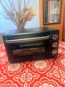 Oster convection toaster oven in matte black features multiple cooking dials on the right side.