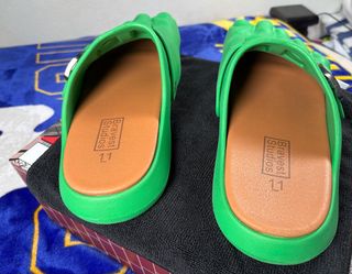These are Bravest Studios Green Hulk Foot Clogs, featuring a molded green design with an adjustable metal buckle.
