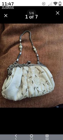 vintage-style ivory fabric evening bag features an ornate, antique-finish metal kiss-lock frame and a beaded top handle.