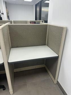 Office cubicle workstation with desk surface and power outlet.