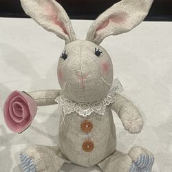 Fabric decorative weighted bunny holding a pink rose with button accents.