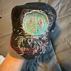 black distressed cadet-style cap featuring a rhinestone-embellished peace sign and embroidered wing details