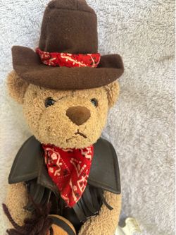 This vintage cowboy teddy bear is likely a collectible produced by Burton + Burton.
