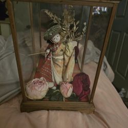 A Japanese doll, likely a Geisha doll, displayed within a glass and wooden case.