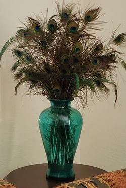 Translucent teal glass vase filled with natural peacock feathers