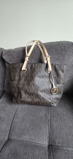 Spacious Michael Kors tote bag has signature brown monogram coated canvas with tan leather straps. Gold-tone MK charm and hardware are attached. Inter