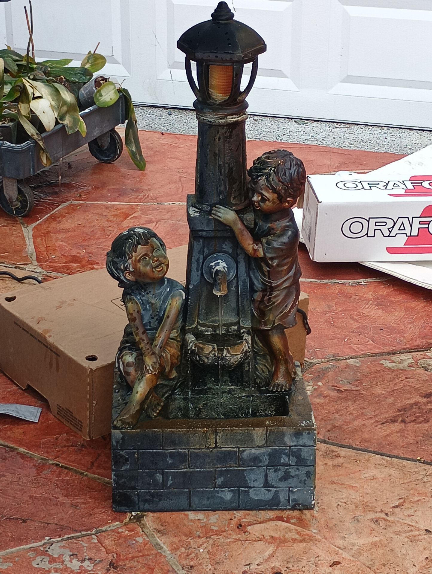 Hi-Line Gift resin outdoor fountain featuring two children playing by a lamppost.
Design Details: The fountain features a playful scene of a boy and