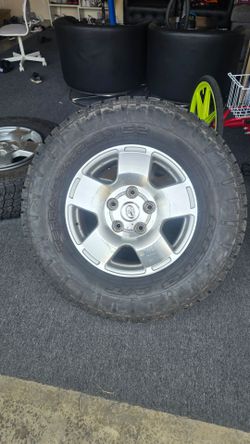 Silver Toyota alloy wheel with a 5-lug pattern and center cap. Shows surface scratches and dirt around the lug holes and spokes. LT285/75R18 129/126R
