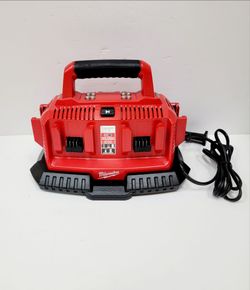 Milwaukee M18 Six-Pack Sequential Charger is red and black with six charging bays. This unit has a top carry handle and a pass-through plug on the pow
