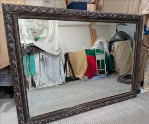 Large beautifully carved ornate beveled mirror with intricate leaf design with a dark finish.