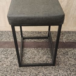 square bar stool with a gray upholstered seat and black metal frame. 