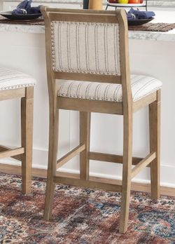 Linon Emmy or Stella grey wash wood counter stool with a striped fabric upholstered seat and brushed silver nailheads. 