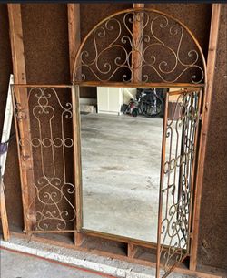 decorative metal arched garden gate wall mirror with opening scrollwork shutters.