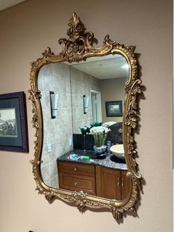 Vintage French Rococo style mirror features an ornate gold-gilded frame with intricate floral and scroll carvings.